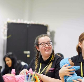 Early Years students sat in classroom smiling holding doll babies